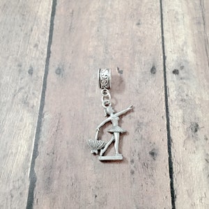 May include: Silver charm featuring a ballerina holding a fan. The charm is attached to a silver chain with a decorative bead.