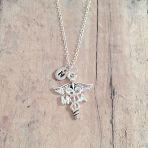 May include: Silver necklace with a medical caduceus charm and a small letter 'N' charm.