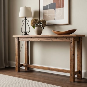 Könnte beinhalten: Ein rustikaler Holztisch mit rechteckiger Platte und vier stabilen Beinen. Auf dem Tisch stehen eine Lampe mit beigem Schirm, eine Vase mit Trockenblumen und eine Holzschale. Der Tisch ist etwa 152 cm lang.