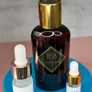 May include: A dark brown bottle with a gold cap and a label that reads "BSB Luxury Coded" is flanked by two smaller glass bottles with white droppers. One bottle is labeled "5 ML" and the other "3 ML".