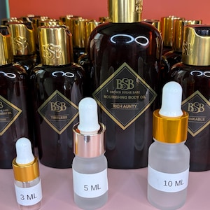 May include: A collection of brown glass bottles with gold-colored lids and labels. The bottles are labeled "Brown Sugar Babe Nourishing Body Oil" and include sizes of 3 mL, 5 mL, and 10 mL. The text "Rich Aunty" is visible on one label.