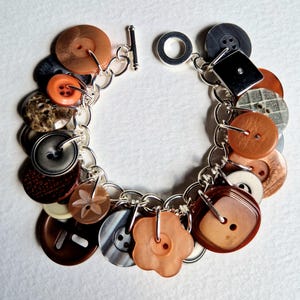 May include: A silver chain bracelet featuring an assortment of colourful buttons. The buttons are in various shapes and sizes, including round, square, and flower-shaped. The bracelet is a great way to add a touch of personality to any outfit.