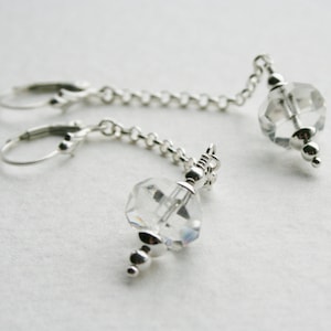May include: A pair of silver earrings with clear crystal teardrop-shaped pendants hanging from delicate chains.