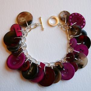 May include: A silver chain bracelet with a variety of colorful buttons, including pink, brown, and black. The buttons are arranged in a cascading pattern.
