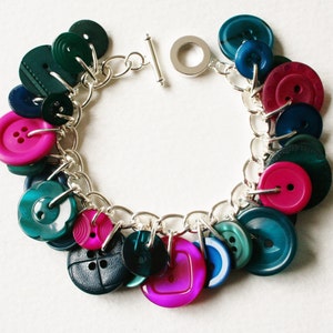 May include: A silver chain bracelet with a variety of colorful buttons, including teal, pink, and red.