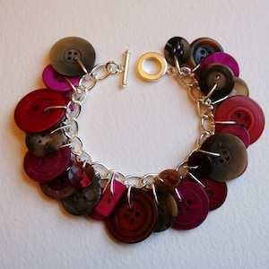 May include: A silver chain bracelet with a variety of colorful buttons, including red, pink, and black. The buttons are attached to the chain with silver rings.