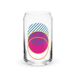 May include: A clear glass can with a pink, yellow, and blue geometric design. The design features a pink circle with yellow and blue stripes inside a larger blue circle with yellow stripes.