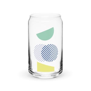May include: A clear glass can with a geometric design. The design features a yellow rectangle, a blue and white striped circle, and a green half-circle.