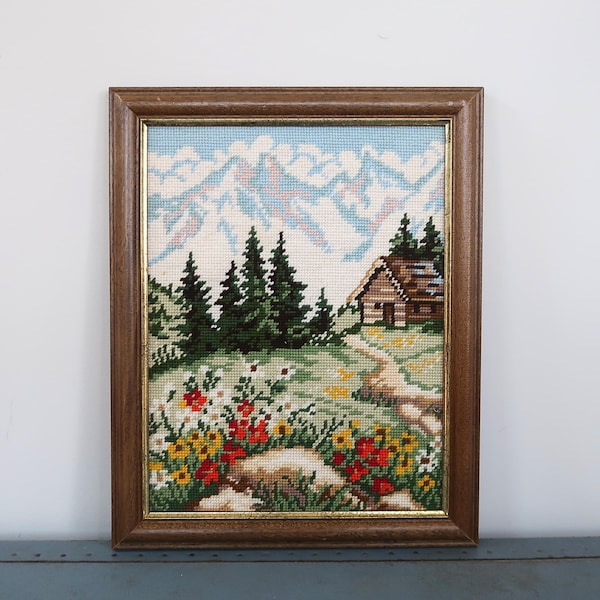 Arte vintage de cabaña alpina bordado con marco, gran paisaje de montaña, decoración de árboles de hoja perenne y flores silvestres.