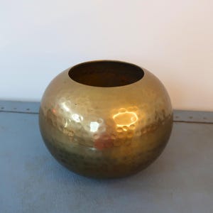 Op de afbeelding: Een gehamerde messing kom met een bolvorm. De kom heeft een brede opening en een getextureerd oppervlak. Het messing heeft een warme, gouden kleur en reflecteert licht.