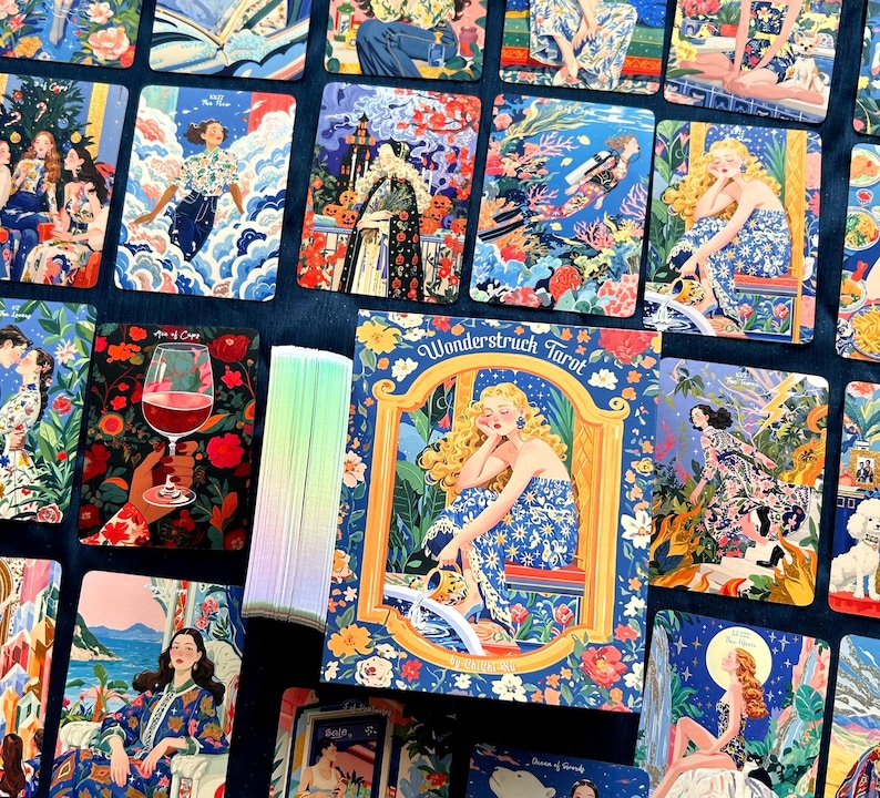 Pode incluir: Um baralho de cartas de tarot Wonderstruck com ilustra&ccedil;&otilde;es coloridas e detalhadas de figuras em v&aacute;rios cen&aacute;rios. A caixa exibe uma figura loira com um vestido floral azul, e as bordas das cartas mostram um gradiente de cores pastel.