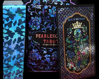 Pode incluir: Um baralho de tarot Pearlescent de Amutey Decu, com uma caixa preta com padrões florais iridescentes e uma carta do Rei de Ouros exibindo uma ilustração de um touro com uma coroa e uma moeda, além de uma borda de carta holográfica azul.