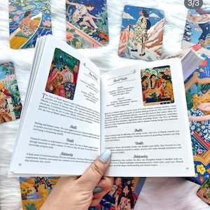 Pode incluir: Um guia aberto para um baralho de tarot, exibindo as p&aacute;ginas 42 e 43 com texto intitulado Five of Wands e Four of Wands. As p&aacute;ginas apresentam ilustra&ccedil;&otilde;es coloridas de pessoas em v&aacute;rias cenas. V&aacute;rias cartas de tarot est&atilde;o espalhadas.