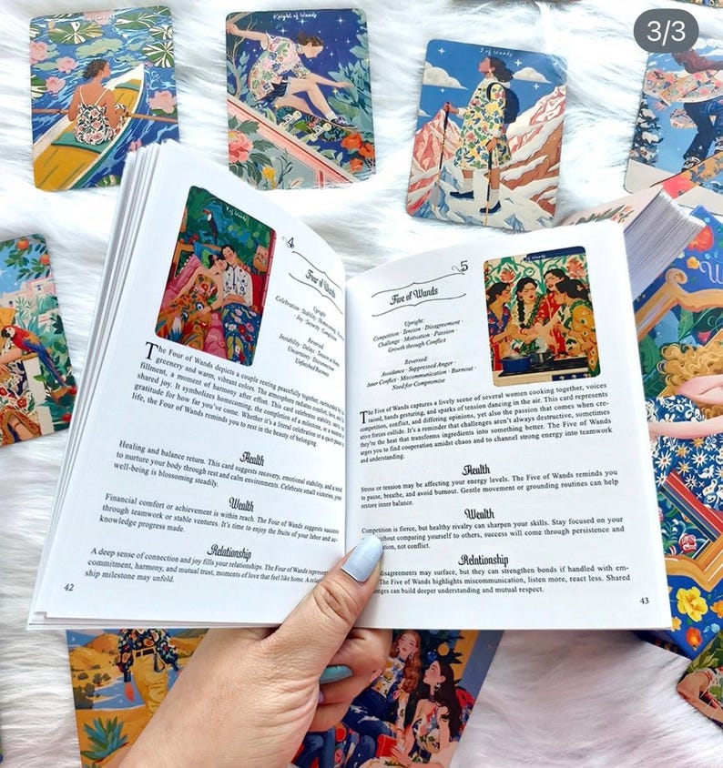 Pode incluir: Um guia aberto para um baralho de tarot, exibindo as p&aacute;ginas 42 e 43 com texto intitulado Five of Wands e Four of Wands. As p&aacute;ginas apresentam ilustra&ccedil;&otilde;es coloridas de pessoas em v&aacute;rias cenas. V&aacute;rias cartas de tarot est&atilde;o espalhadas.