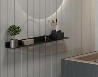 May include: A long, thin, black metal wall-mounted shelf holds a small potted green plant, a rectangular beige container, a small black jar, and a black cup containing two wooden toothbrushes, positioned against a vertical paneled wall.
