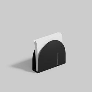 May include: A black napkin holder with a semi-circular design, holding a stack of white napkins. The holder has a vertical slit on the front. The design is minimalist and modern, suitable for a kitchen or dining room.