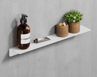 May include: White wall-mounted shelf with rounded edges, featuring a brown glass bottle with a pump dispenser, a tube of hand cream, and two brown ceramic containers. One container has a small plant growing out of it.