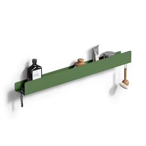 Puede incluir: Una estantería de pared larga y estrecha de metal verde oliva con respaldo plano y borde frontal. La estantería sostiene una botella oscura con etiqueta blanca, un cepillo de madera, un tubo plateado, un frasco pequeño y un cepillo colgante.
