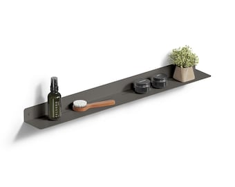 Può includere: Una lunga mensola da parete in metallo grigio scuro con un design a fessure orizzontali. La mensola ospita un flacone spray in vetro scuro, una spazzola con manico in legno, due piccoli contenitori neri e una piccola pianta verde in vaso beige.