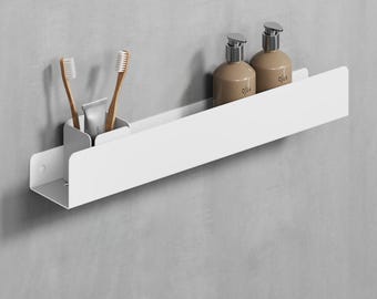 May include: White metal bathroom shelf with two brown bottles labelled "Olja" and a compartment for toothbrushes and toothpaste.