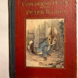 Könnte beinhalten: Ein antikes Buch mit dem Titel "Children's Hour with Peter Rabbit". Der rote Einband trägt goldene Buchstaben und eine gerahmte Illustration von Peter Rabbit in einem blauen Jackett. Der Buchrücken ist verblasst blau.