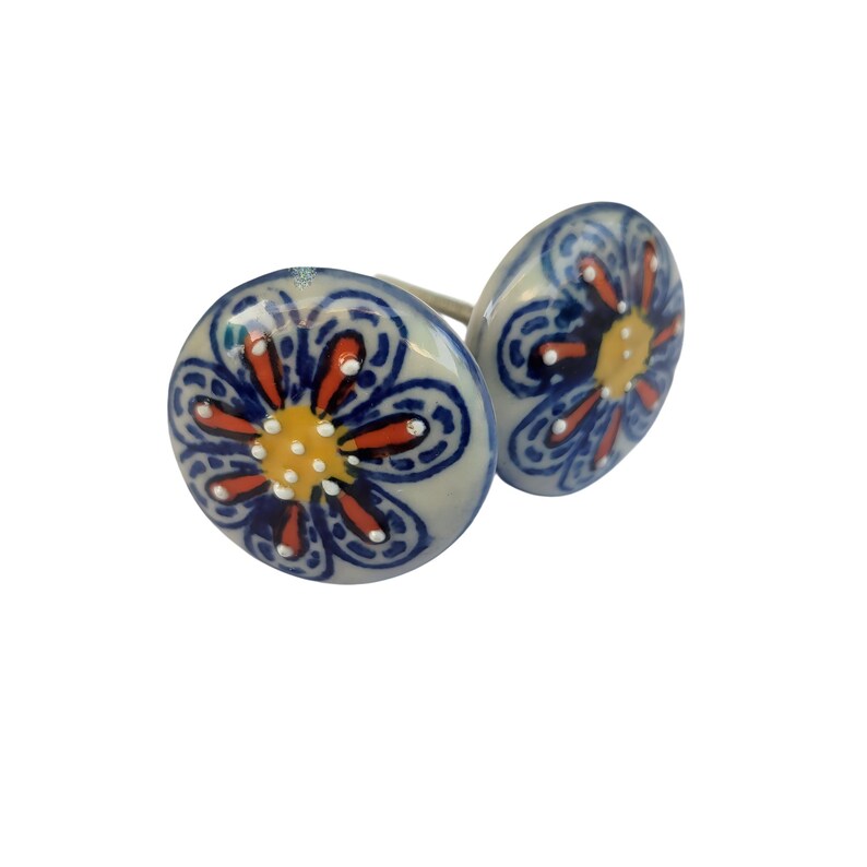 May include: Two ceramic cabinet knobs with a floral design. The knobs are white with a blue floral pattern, orange accents, and a yellow center. The knobs are round and have a metal stem for installation.