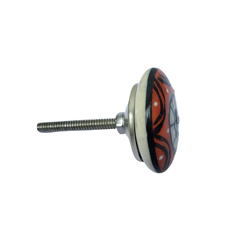 May include: A decorative ceramic cabinet knob with a metal screw. The knob features a design with red, black, and white colors. The knob is round and has a floral pattern.
