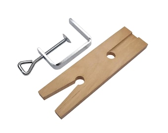 May include: A silver metal clamp with a wooden base. The base has two holes for holding rings or other jewelry.