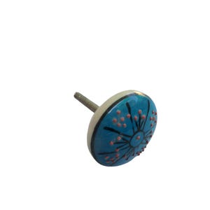 May include: A round, ceramic cabinet knob with a blue and cream color scheme. The knob features a blue face with a black and orange floral design. The threaded bolt is silver.