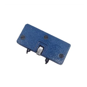 Peut inclure: Un ouvre-boîte de montre en métal bleu avec un bouton argenté et deux pointes. L'ouvre-boîte a quatre vis sur le dessus et le dessous.