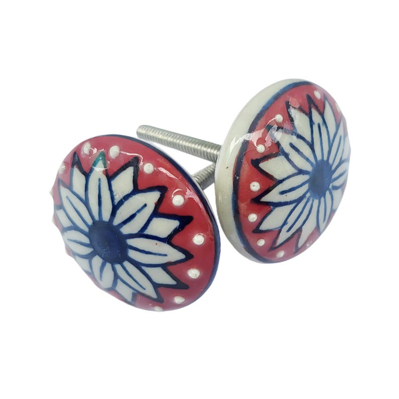 May include: Two decorative ceramic cabinet knobs. Each knob features a floral design with white petals, a blue center, and a red background with white dots. The knobs have a silver screw for installation.