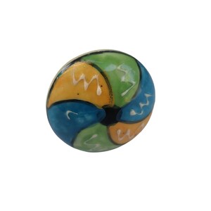 Pode incluir: Um puxador decorativo redondo e colorido com acabamento brilhante. O puxador apresenta um design segmentado com sec&ccedil;&otilde;es azuis, verdes e amarelas, acentuadas com ziguezagues brancos. O centro &eacute; preto. Este puxador &eacute; provavelmente para m&oacute;veis.