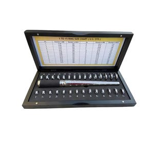 May include: A wooden box containing a ring sizer tool and a set of 15 ring sizing gauges. The box has a chart on the inside with ring sizes in millimeters and inches. The chart is labeled "1 to 15 Ring Size Chart (U.S. STD.)"