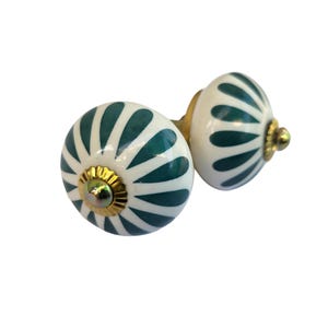 May include: Two decorative cabinet knobs. Each knob is a white sphere with teal-colored, petal-like designs. The knobs have gold-colored metal accents and are designed for easy installation. These knobs are a stylish addition to any cabinet or drawer.