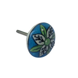 May include: A decorative ceramic cabinet knob with a floral design. The knob features a white flower with green leaves on a blue background. The knob has a metal screw for installation.