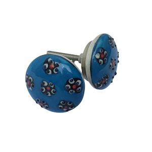 May include: Two blue ceramic cabinet knobs with a floral pattern. Each knob has a glossy finish and is decorated with black, red, and white flower-like designs. The knobs are mounted on a silver metal screw.