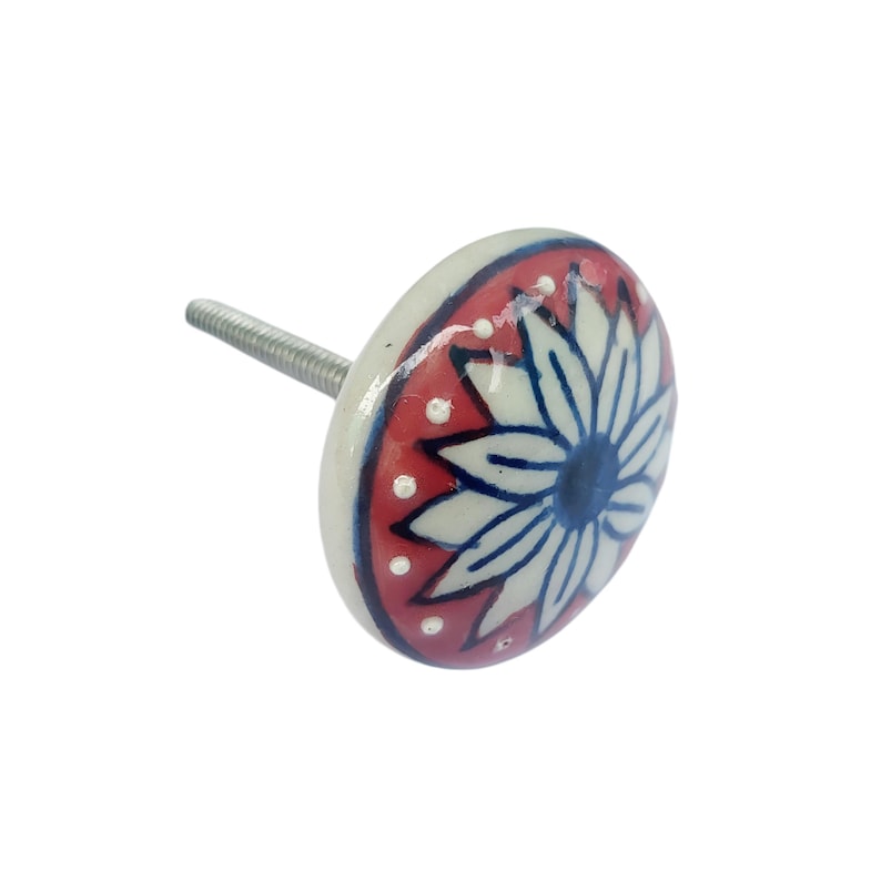 May include: A decorative ceramic cabinet knob with a floral design. The knob features a white flower with blue details on a red background, accented with white dots. The knob has a silver metal screw for attachment.