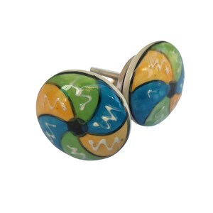 May include: Two colorful ceramic cabinet knobs. Each knob is round with a silver metal base and screw. The knobs feature a design of blue, green, yellow, and orange segments with white squiggly lines. The knobs are on a white background.