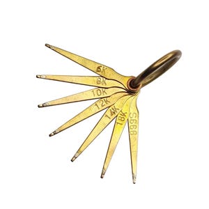 May include: A set of gold-colored feeler gauges attached to a ring. Each gauge is labeled with a number and the letter "K", ranging from 6K to 18K, and one is labeled "S666". The gauges are arranged in a fan shape against a white background.