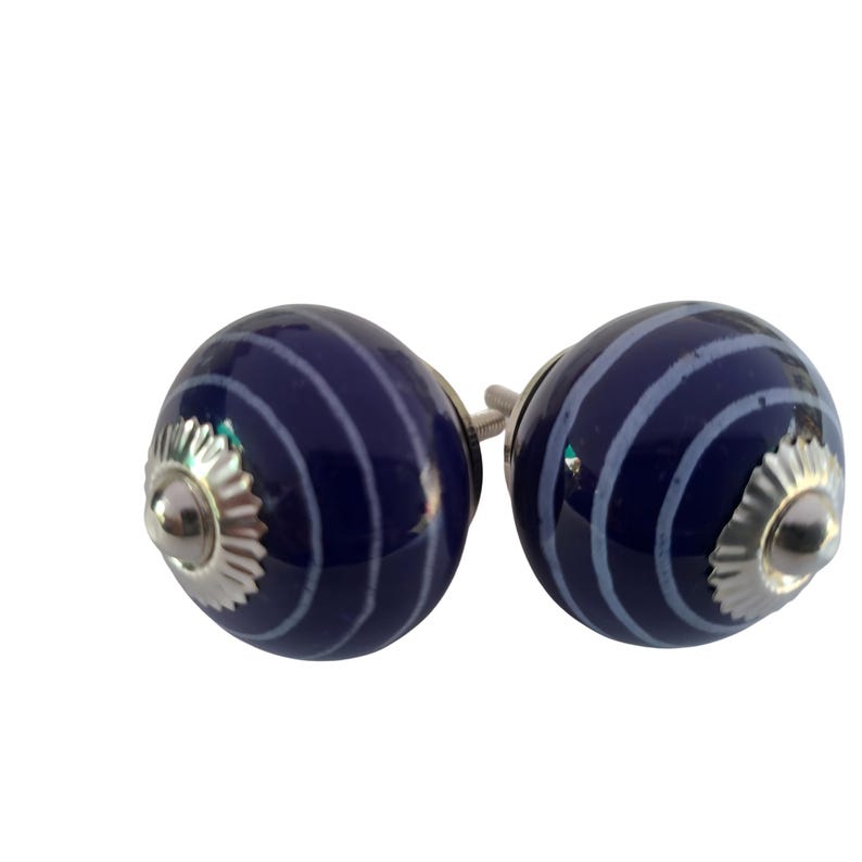 May include: Two navy blue ceramic cabinet knobs with a silver base. Each knob has a series of white curved stripes. The knobs are round and have a glossy finish. These decorative knobs are ideal for furniture.