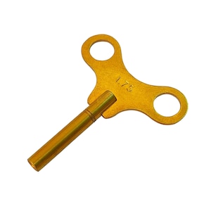 May include: A gold-colored metal wind-up key with a T-shaped handle and a long shaft. The handle has two holes and the shaft is marked "1/75".