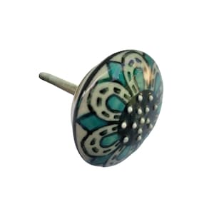 May include: Decorative ceramic cabinet knob with a floral design. The knob features a white, teal, and black colour scheme. The knob has a metal screw for installation. The knob is approximately 3.8 cm in diameter.