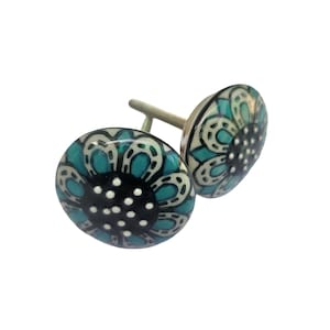 May include: Two decorative ceramic cabinet knobs. Each knob features a teal and white floral design with a black center and white dots. The knobs have a silver-colored screw for mounting. These knobs are perfect for adding a touch of style to any cabinet or drawer.