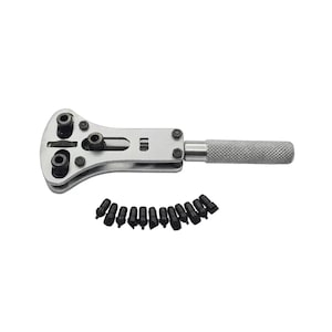 May include: A silver watch case opener with a handle and a removable head with multiple sizes of watch case opening attachments. The tool is laid out on a white background with the attachments arranged in a semi-circle.
