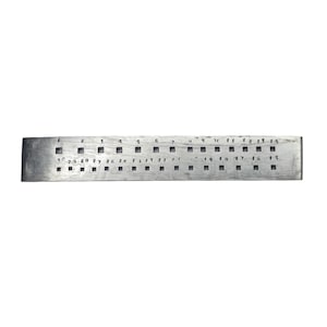 May include: A rectangular metal gauge with square holes and numbers etched above and below. The gauge is silver-toned and has a worn appearance. The numbers are small and evenly spaced, indicating measurements or sizes.
