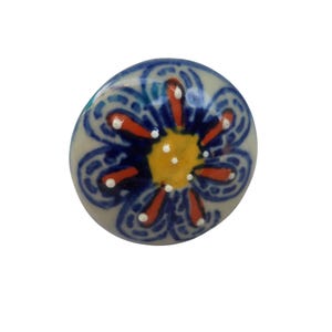 May include: A ceramic cabinet knob with a floral design. The knob features a light gray base with a blue, orange, and yellow flower pattern. The flower has a yellow center, orange petals, and blue accents.