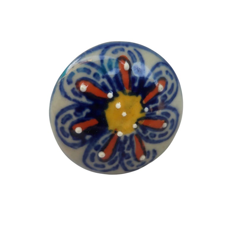 May include: A ceramic cabinet knob with a floral design. The knob features a light gray base with a blue, orange, and yellow flower pattern. The flower has a yellow center, orange petals, and blue accents.