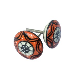 May include: Two decorative ceramic cabinet knobs. The knobs are orange with a black, white, and gray floral design. The knobs have a silver screw for installation. The knobs are a unique accent for any cabinet or drawer.