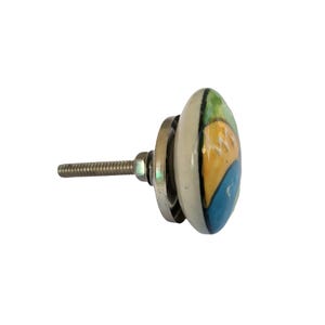 Pode incluir: Puxador de arm&aacute;rio decorativo em cer&acirc;mica com um desenho pintado. O puxador tem uma base branca com um desenho azul, amarelo e verde. O puxador tem uma base e um parafuso de metal prateado para instala&ccedil;&atilde;o.