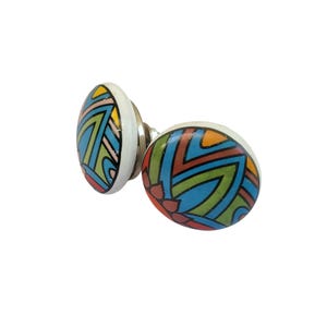 May include: Two decorative cabinet knobs with a white base and colorful geometric patterns. The knobs feature a mix of blue, green, orange, and red designs. The knobs are made of ceramic and have a metal stem.